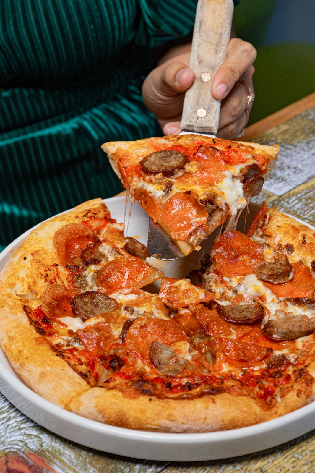 A slice of pepperoni and sausage pizza being lifted from a pie